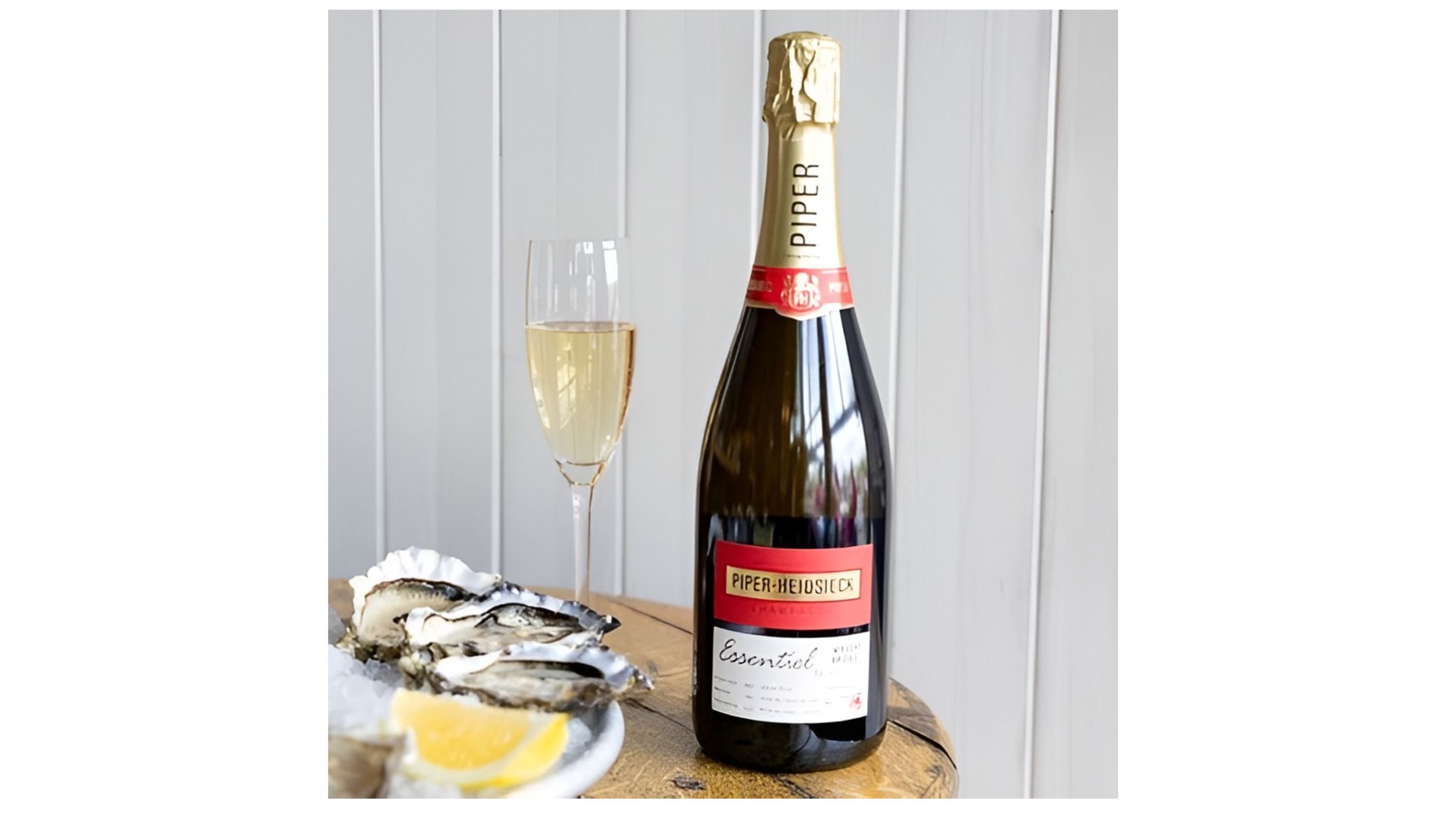 A bottle of Piper-Heidsieck Essentiel champagne and a flute next to a dish of fresh oysters and a lemon wedge.