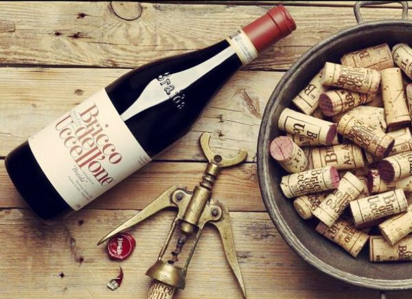 A bottle of Braida Barbera d'Asti Bricco dell'Uccellone 2021 is placed along with other corks on a wooden table.