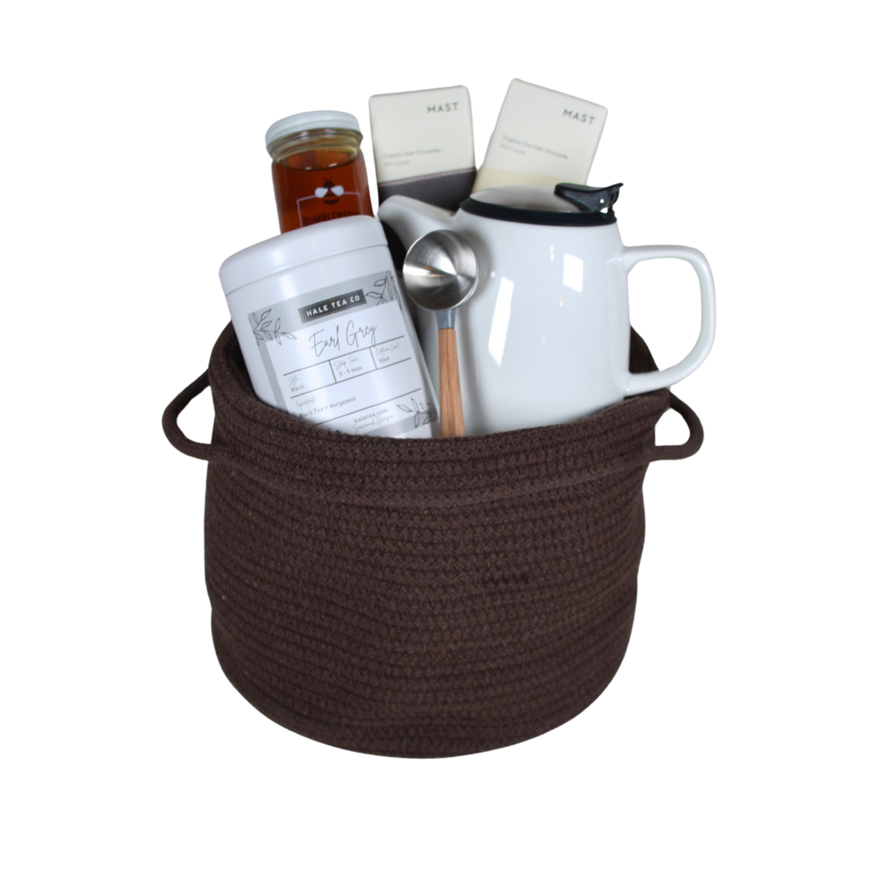 Dark brown rope basket filled with Earl Grey tea, a honey jar, two chocolate bars, a white mug, and a metal tea scoop.