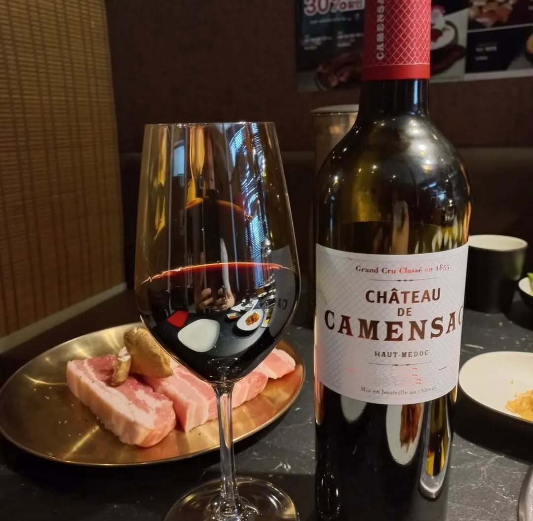 A bottle of 95-point Château Camensac Haut-Médocat 2016, along with some food placed on a table. 