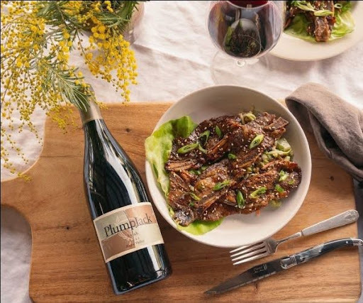 Plumpjack wine bottle beside a plate of grilled seasoned meat garnished with green onions, paired with a glass of red wine.