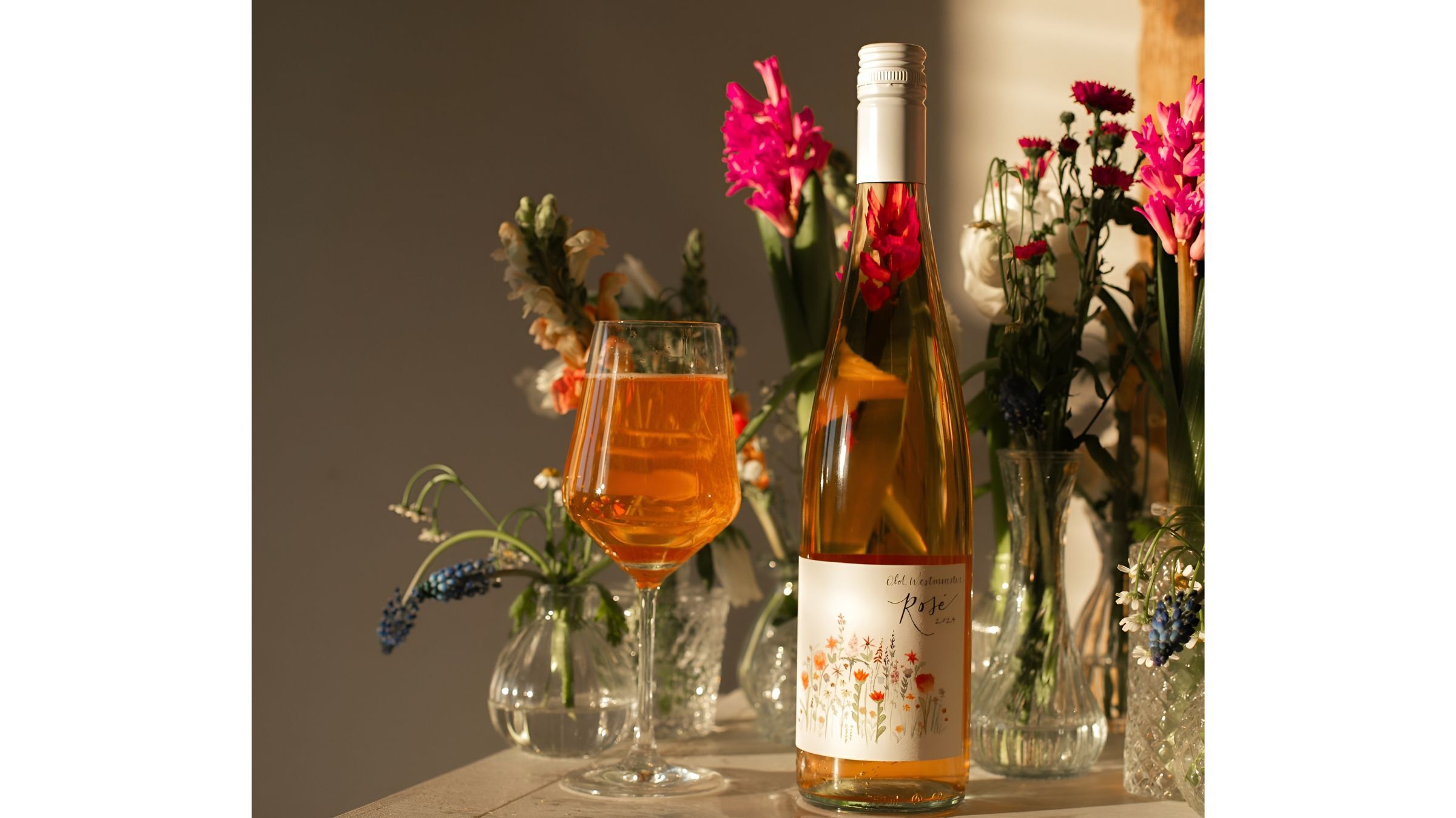 Sparkling rosé wine bottle and glass styled with fresh flowers in warm indoor light.
