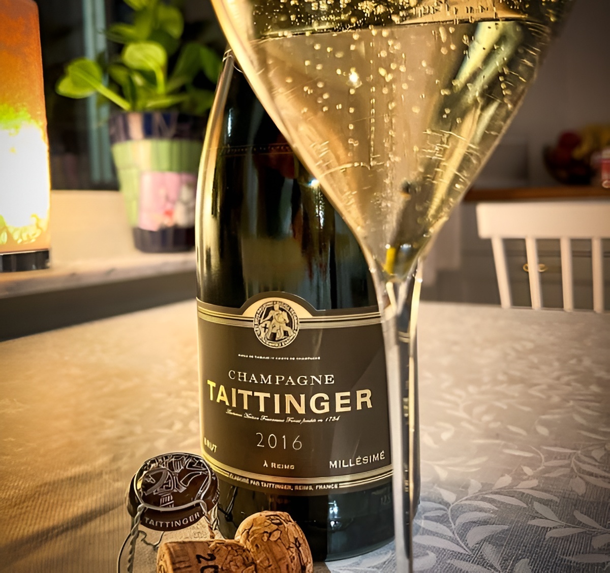 A bottle of Taittinger with a glass of sparkling wine catching warm light and fine bubbles.