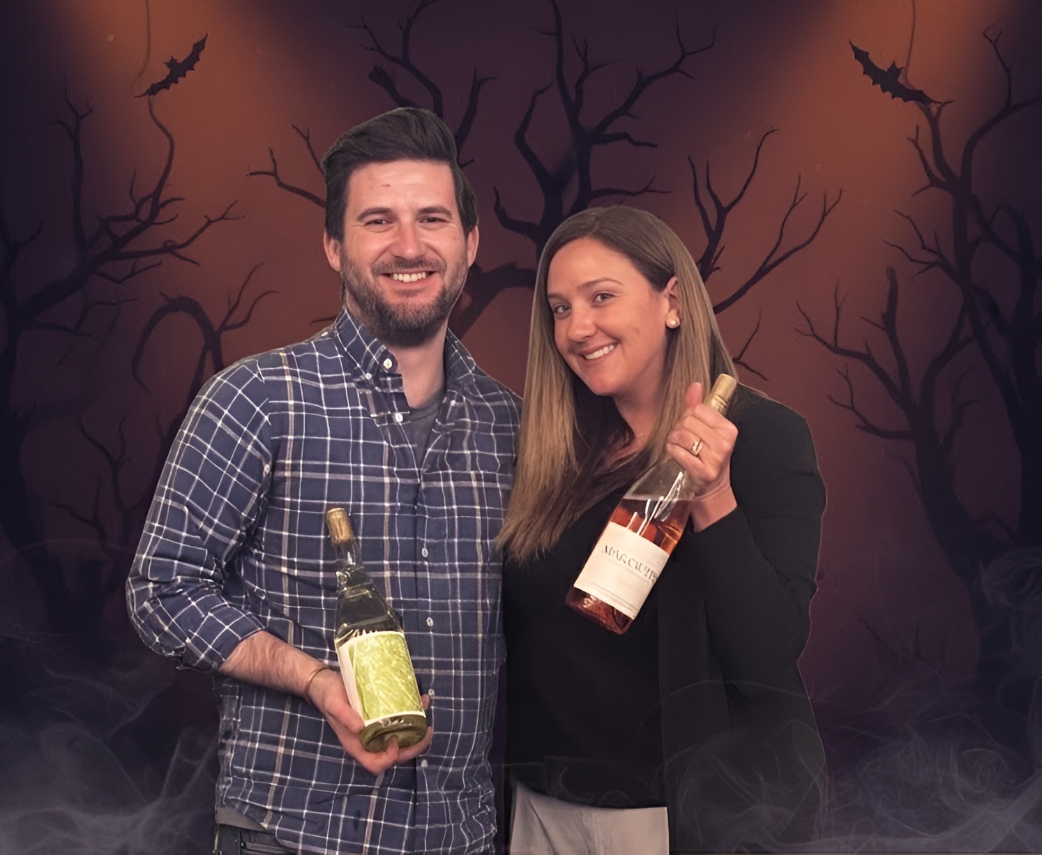 Two people holding wine bottles, posing for the camera at Woodland Hills Wine Company event.