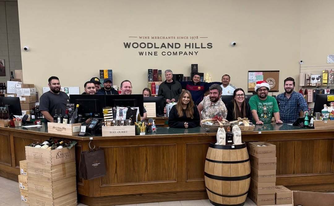 Woodland Hills Wine Company staff standing behind the counter, smiling at the camera.